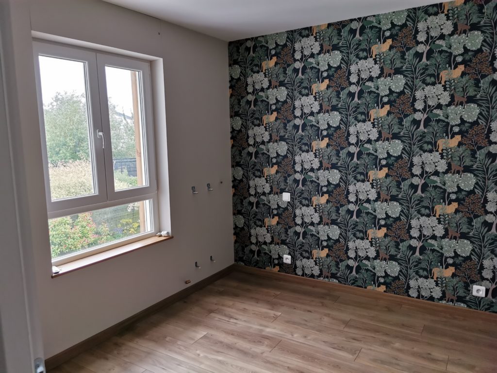 Installation d’un nouveau revêtement mural dans une petite chambre rénovée.