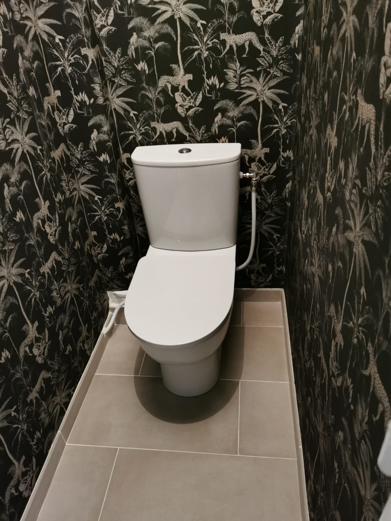 Création d’un WC fonctionnel et moderne avec grand carrelage et décoration papier peint type jungle.