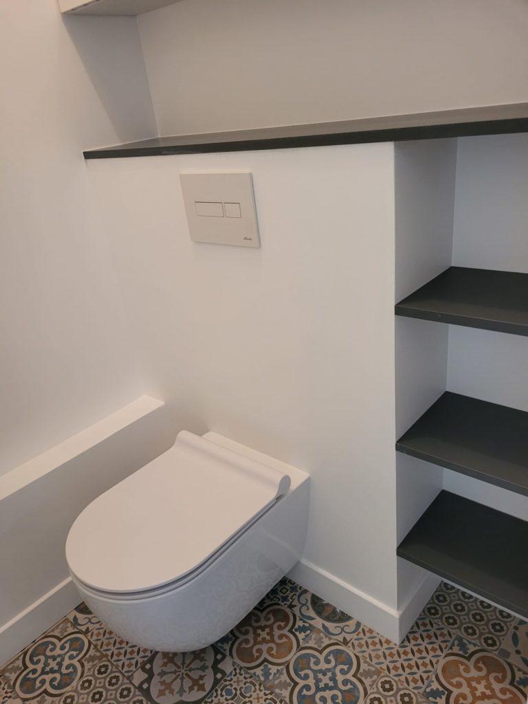 Pose d’un WC suspendu et création d’étagères murales dans un espace sanitaire rénové.