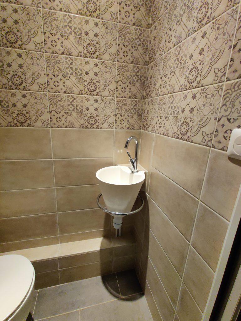 Pose d’un lave-main et installation de carrelages muraux dans un espace WC rénové.