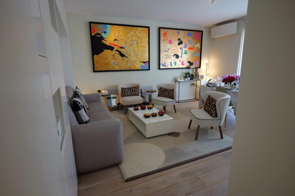 Salon design avec tableau moderne au mur, canapé gris et trois fauteuils blancs pour une ambiance cosy pour l'apéro