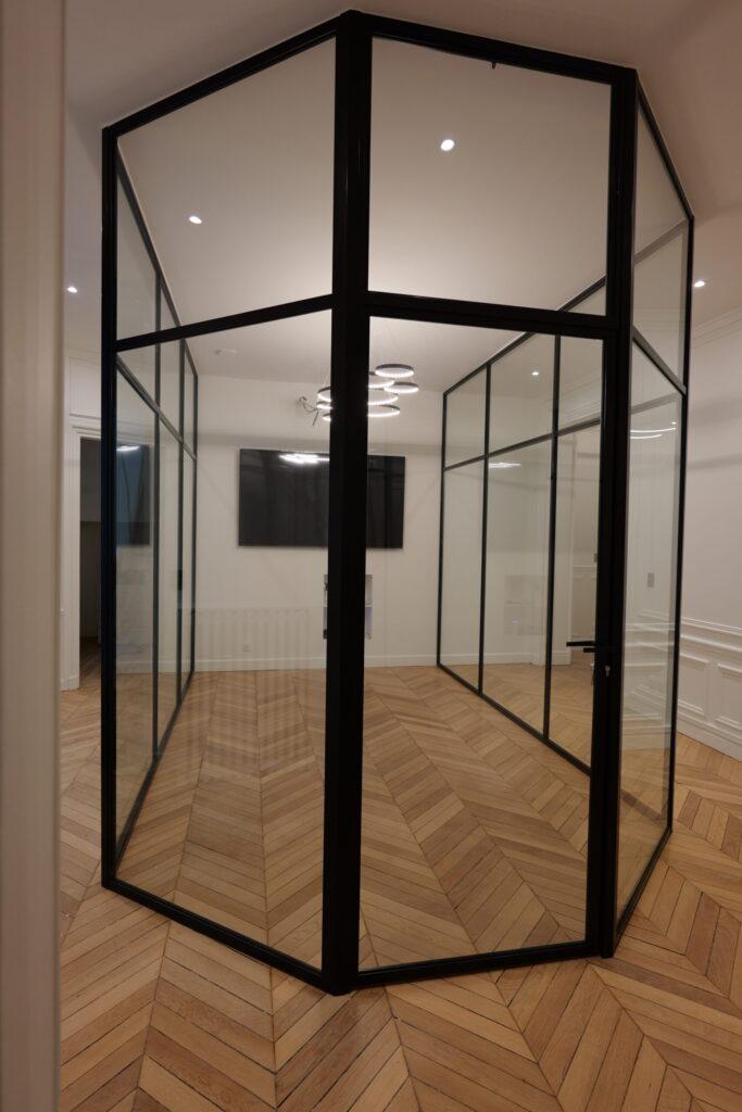 Armature métallique vitrée créant une salle de réunion moderne sur un parquet en pointe de Hongrie