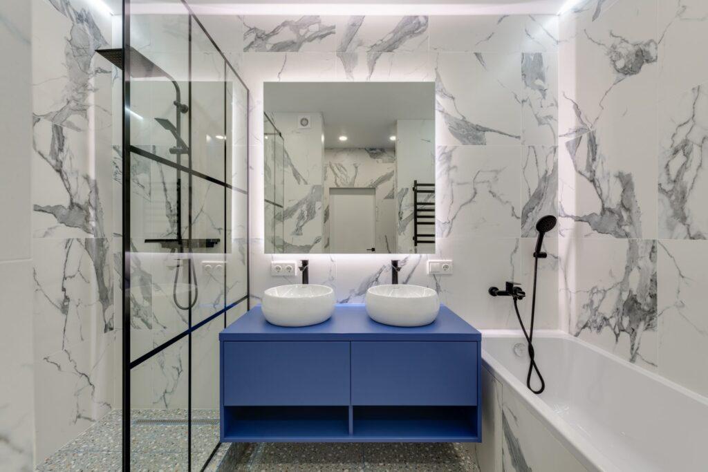 Salle de bain en marbre blanc avec meuble bleu roi, douche à l'italienne et baignoire
